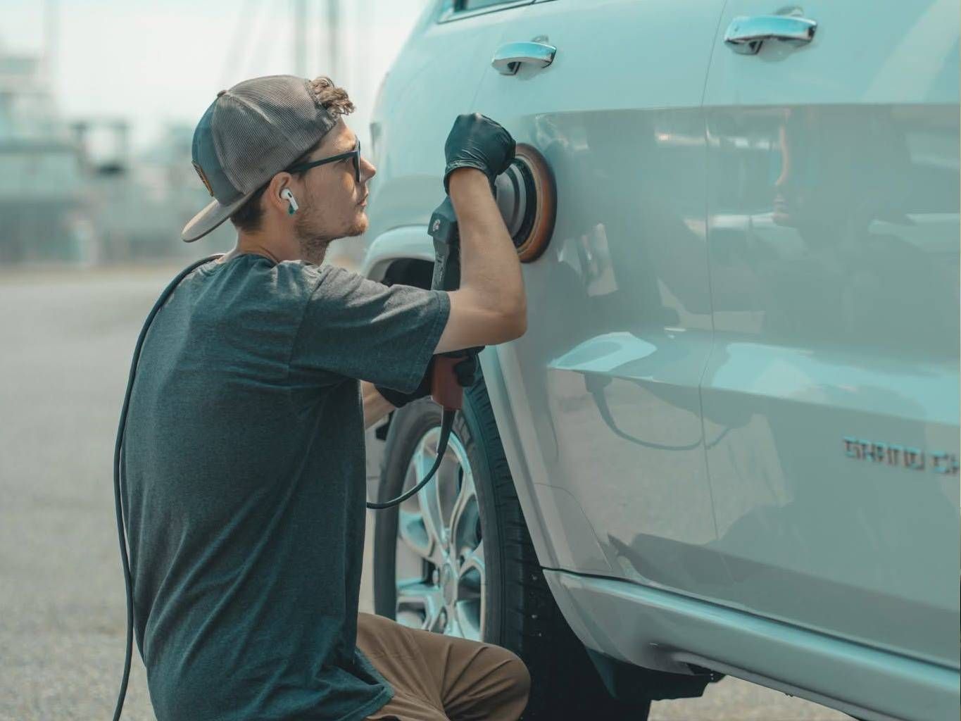 Mechanic polishing the front fender of a light blue car in a workshop