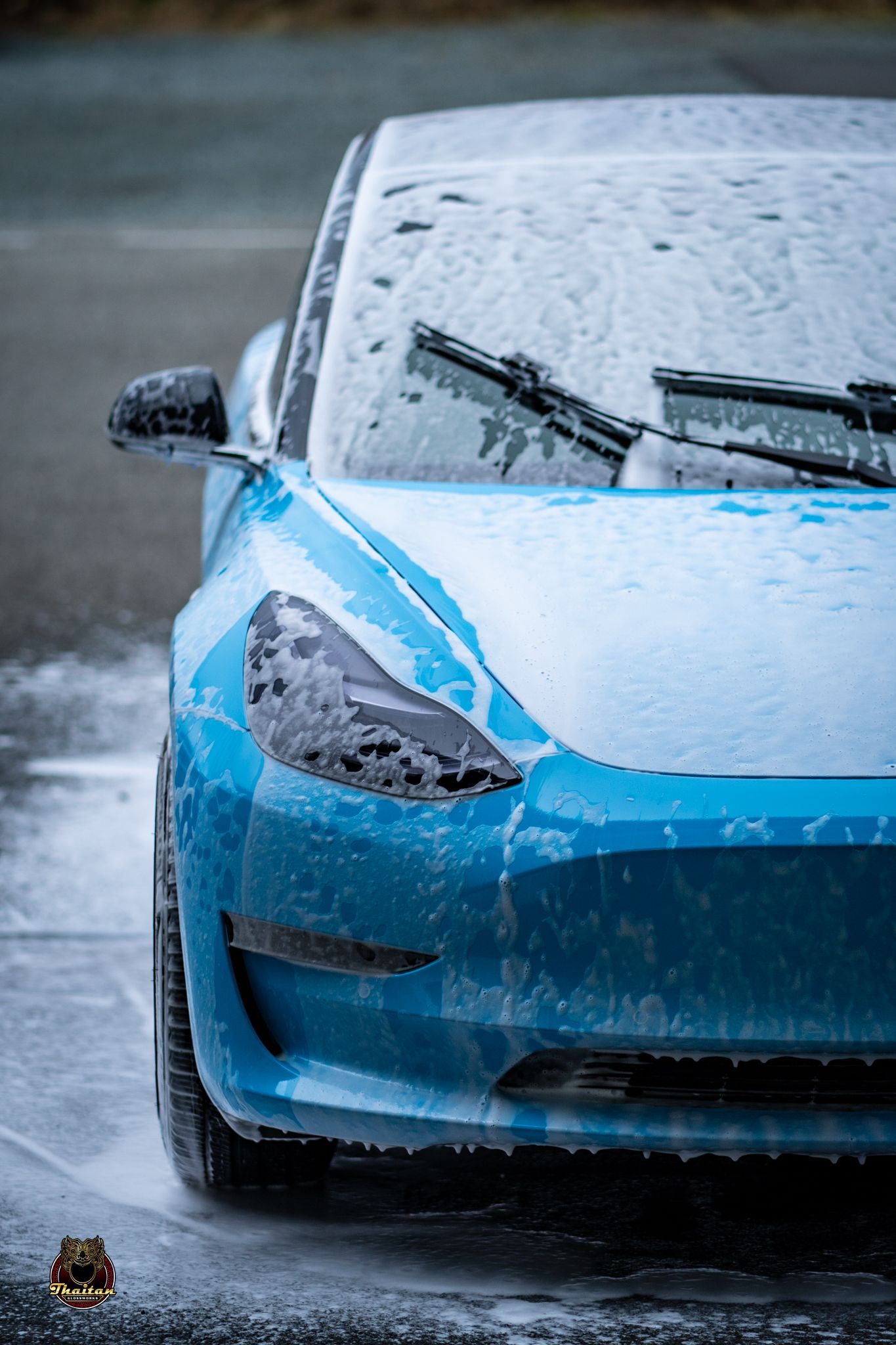 A blue tesla model 3 is being washed with foam.