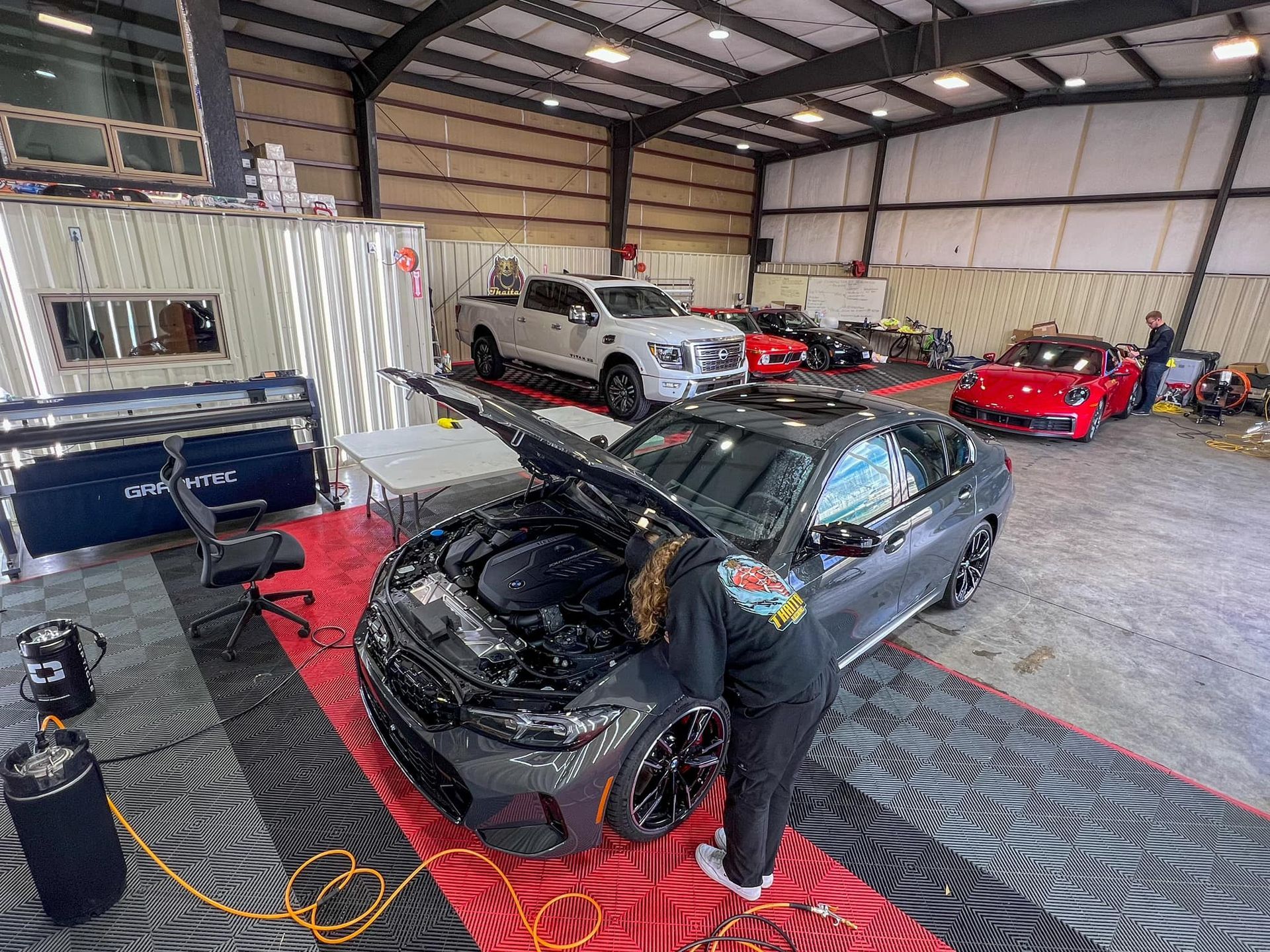 A man is working on a car in a garage with the hood up.