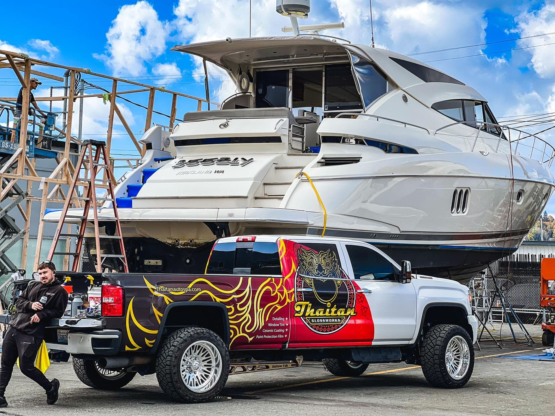 White truck with custom graphics parked near a large yacht; man gestures toward the vehicle.