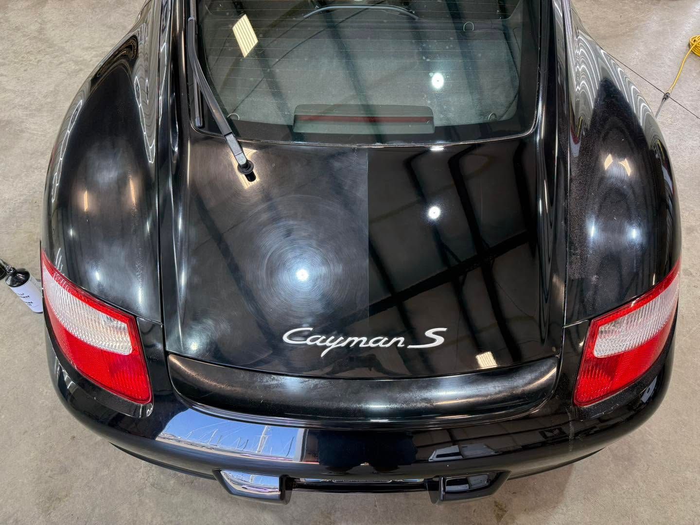 Black Porsche Cayman S seen from the rear, with red taillights in a garage.