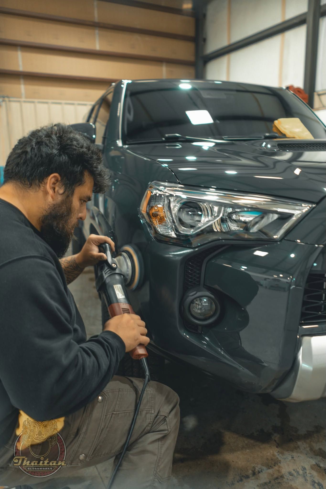 Mechanic polishing the front bumper of a dark SUV in a garage