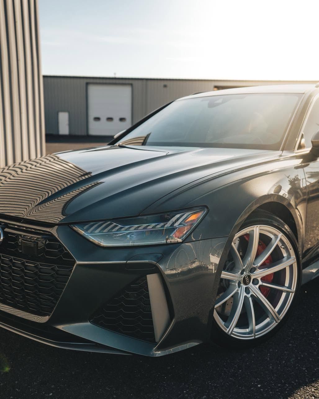 Black sports sedan parked outdoors in sunlight, front-left view with silver rims.