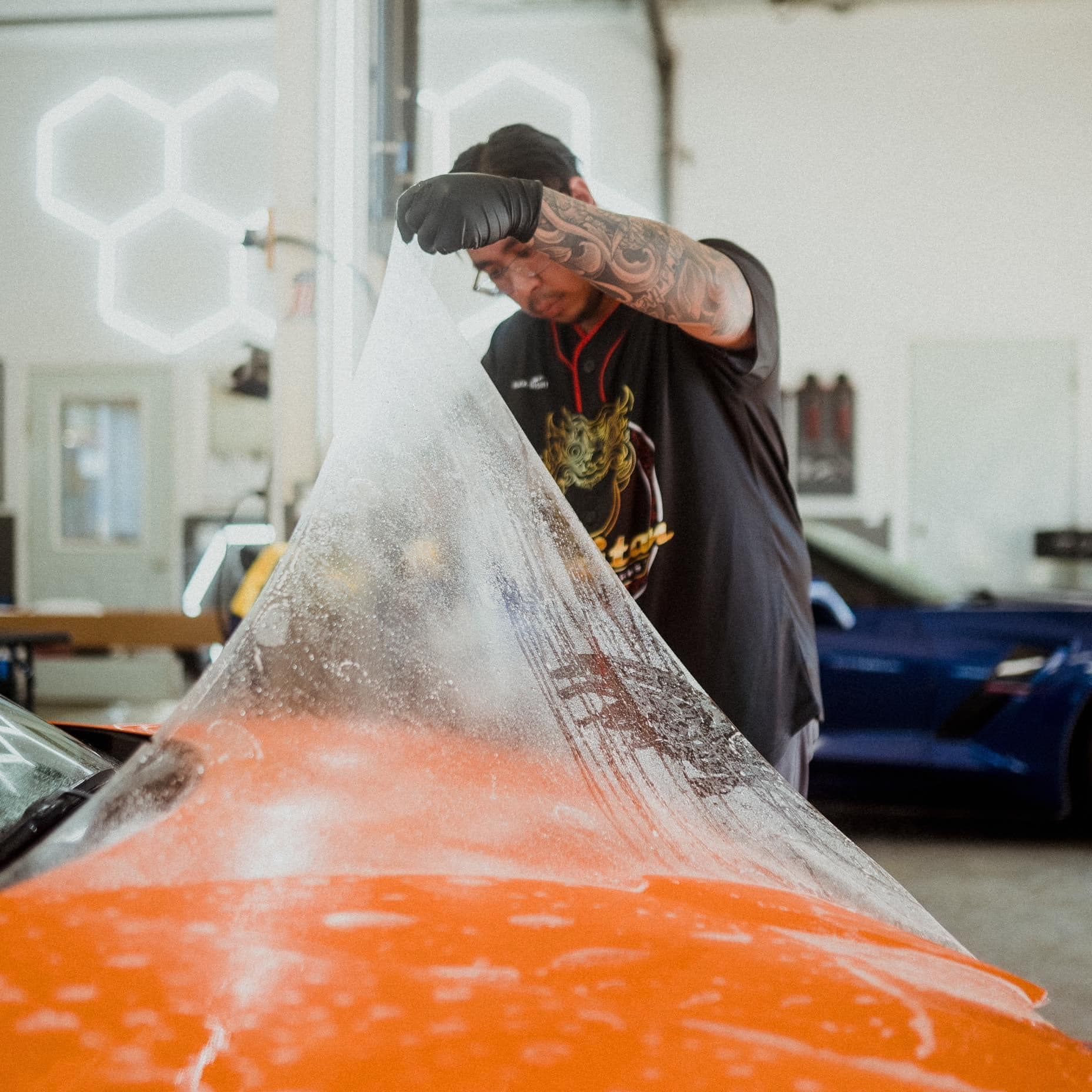A man is wrapping a car with plastic wrap in a garage.