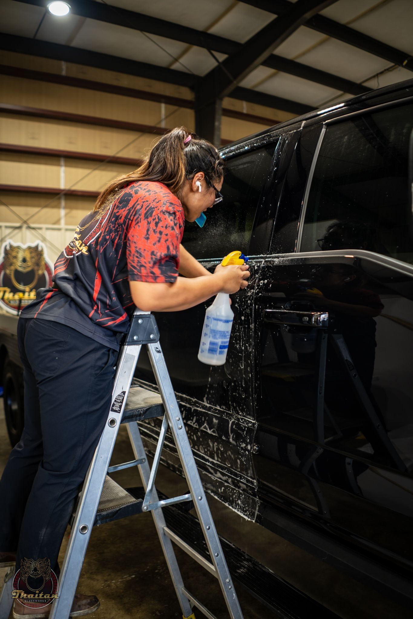 Person cleaning a glossy black vehicle with spray cleaner in a garage.