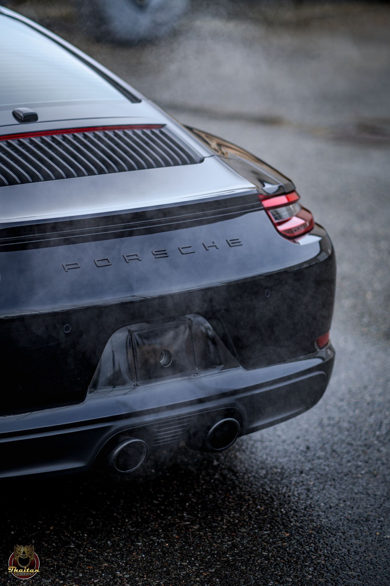 A black porsche 911 is parked on a wet street.