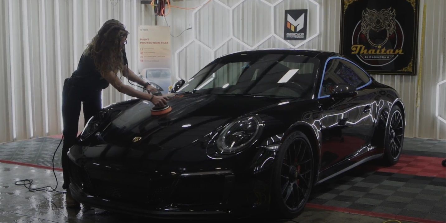 A woman is polishing a black car in a garage.