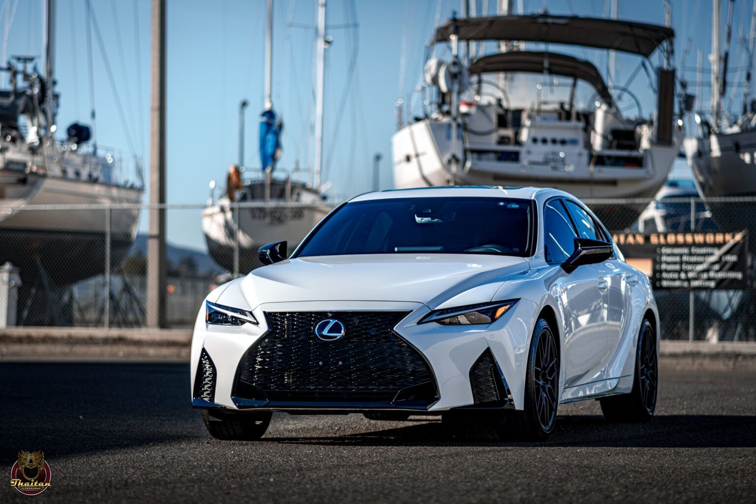White Lexus sedan parked near sailboats on a sunny day.