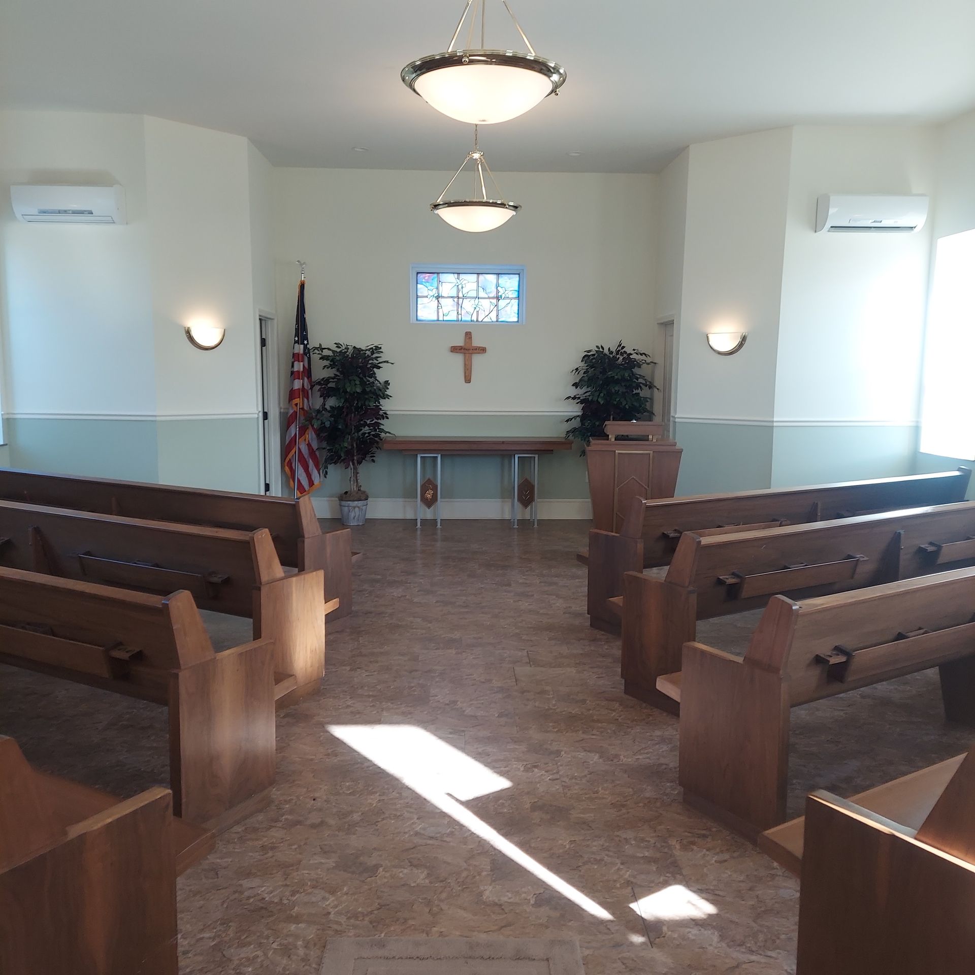 Small chapel interior with wooden pews, altar, cross, and sunlight on the floor.