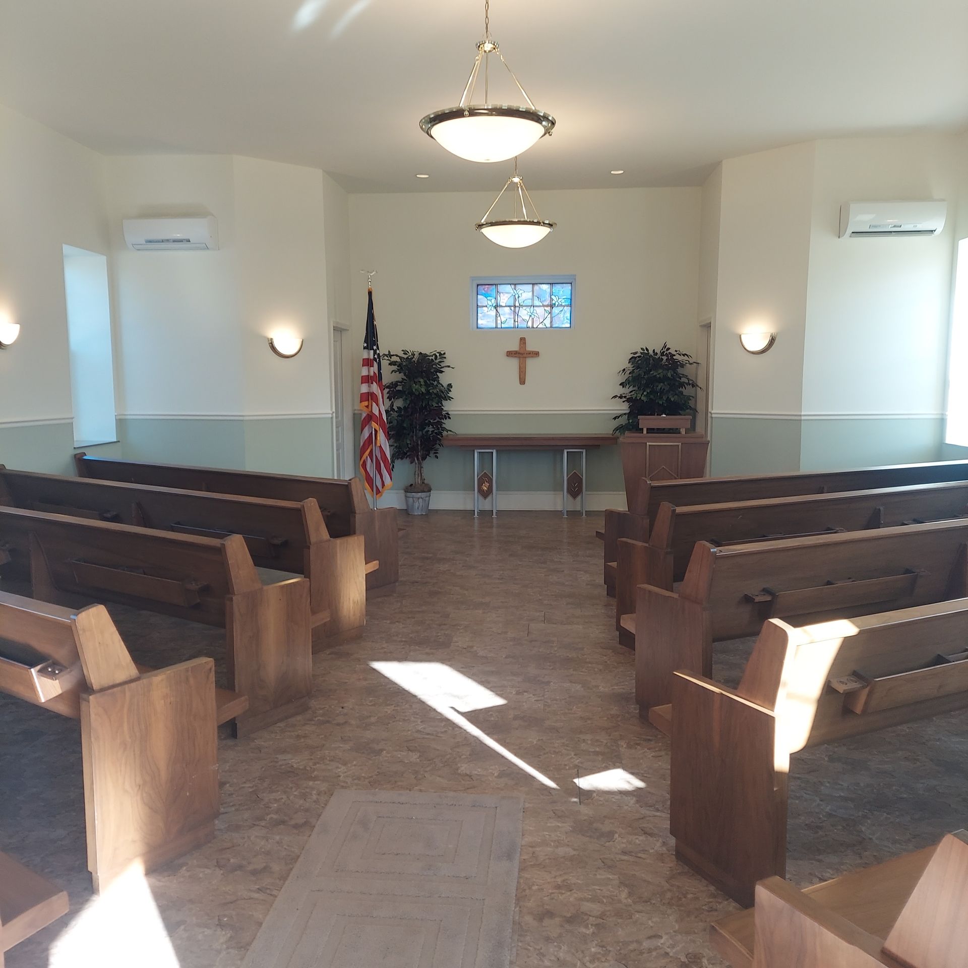 Empty church sanctuary with wooden pews, altar, cross, and stained-glass window