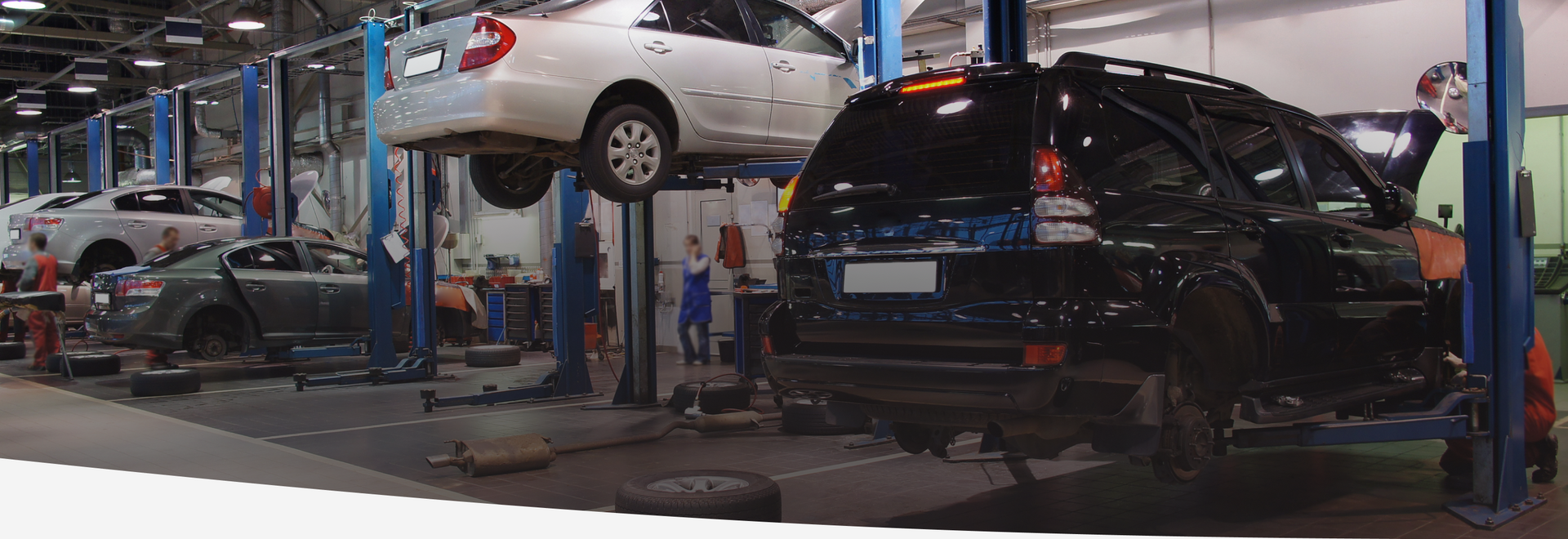 Cars on lifts in a busy auto repair shop, mechanics working on them. | Prestige Tire & Auto