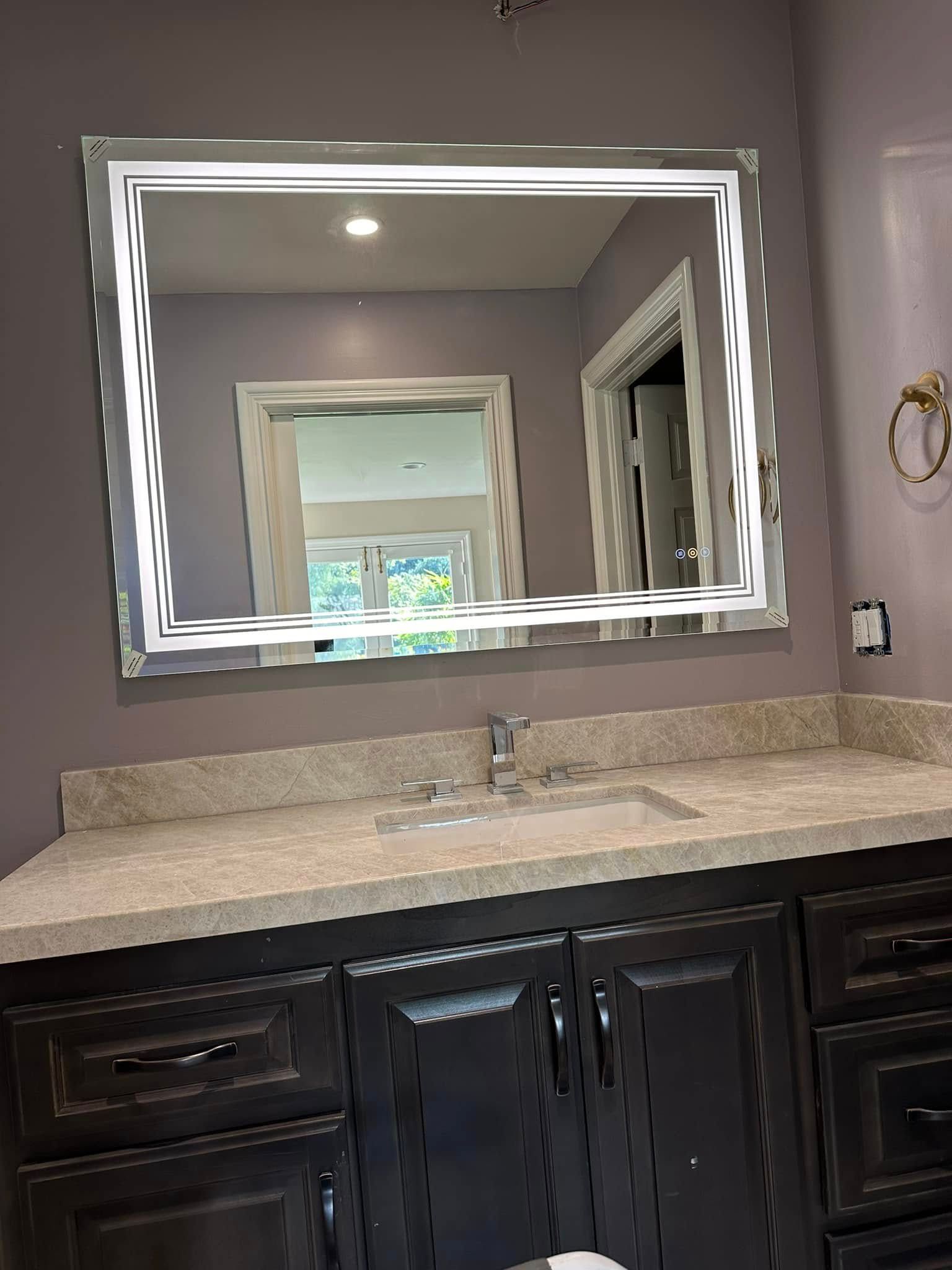 Bathroom vanity with granite countertop, dark cabinets, and a large illuminated mirror over the sink
