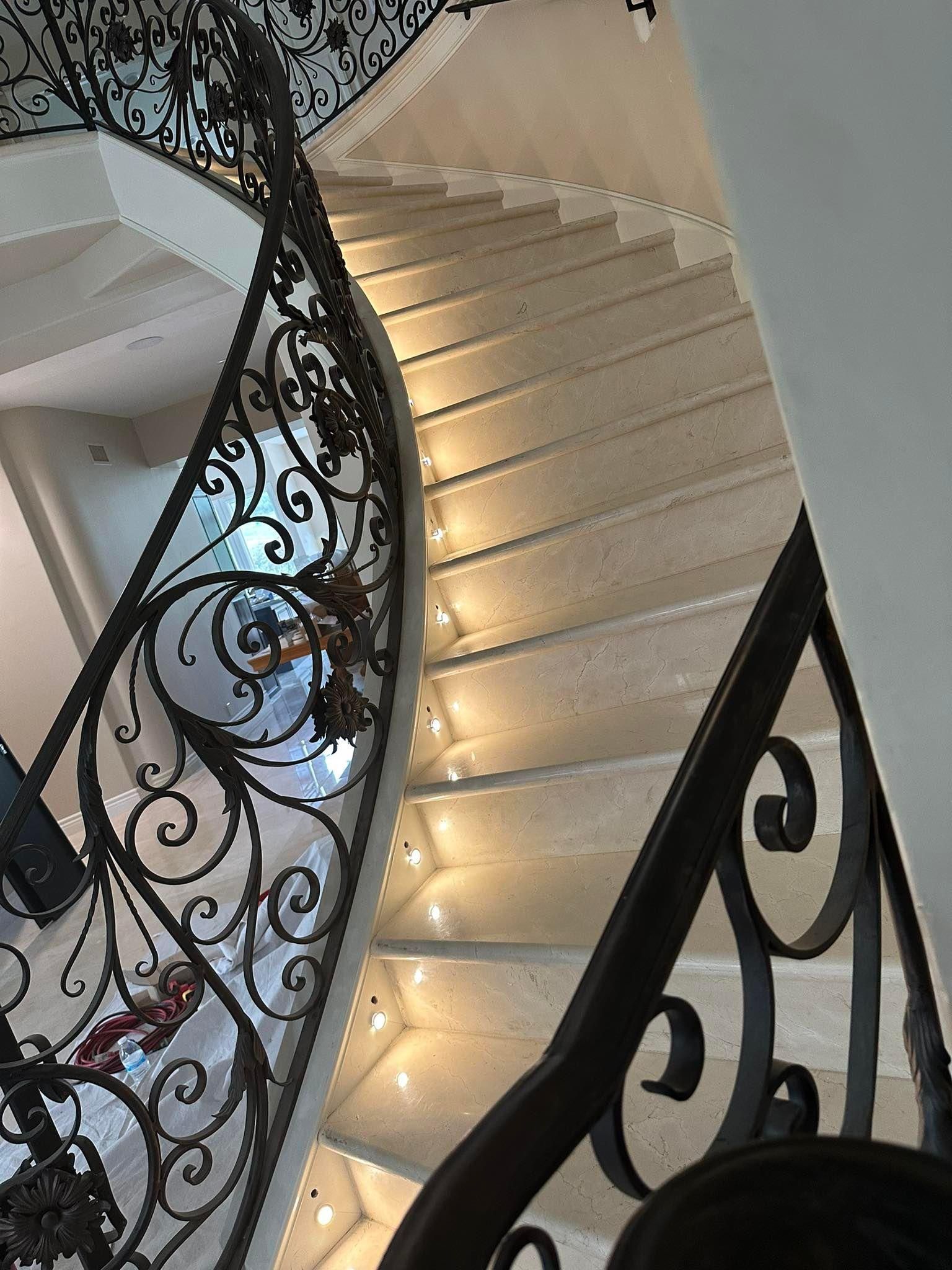 Curved indoor staircase with ornate black railings and warm step lights.