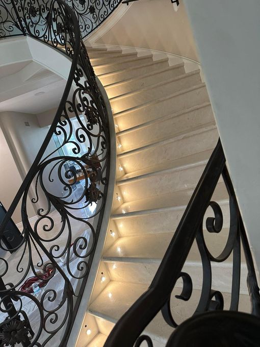 Curved indoor staircase with ornate black wrought-iron railing and warm step lighting