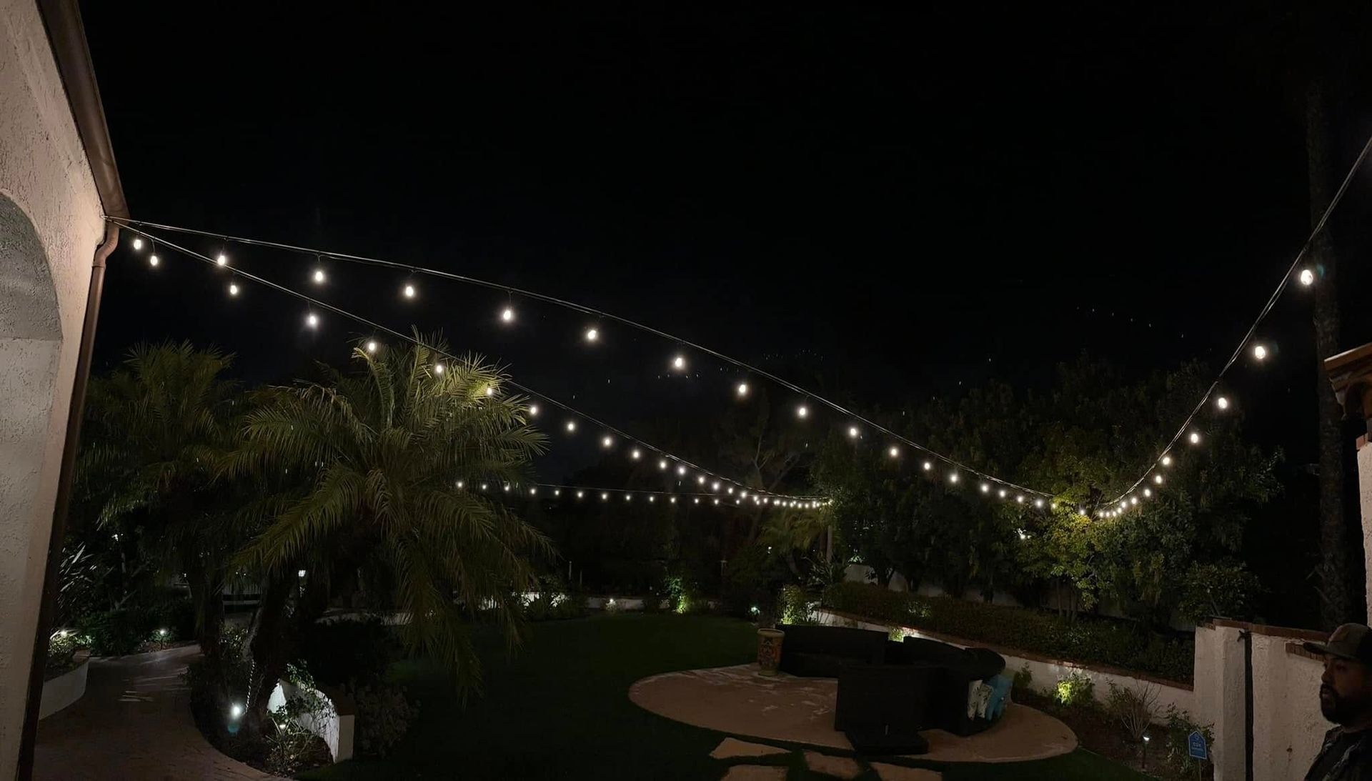 String lights above a patio with palms and a round table at night