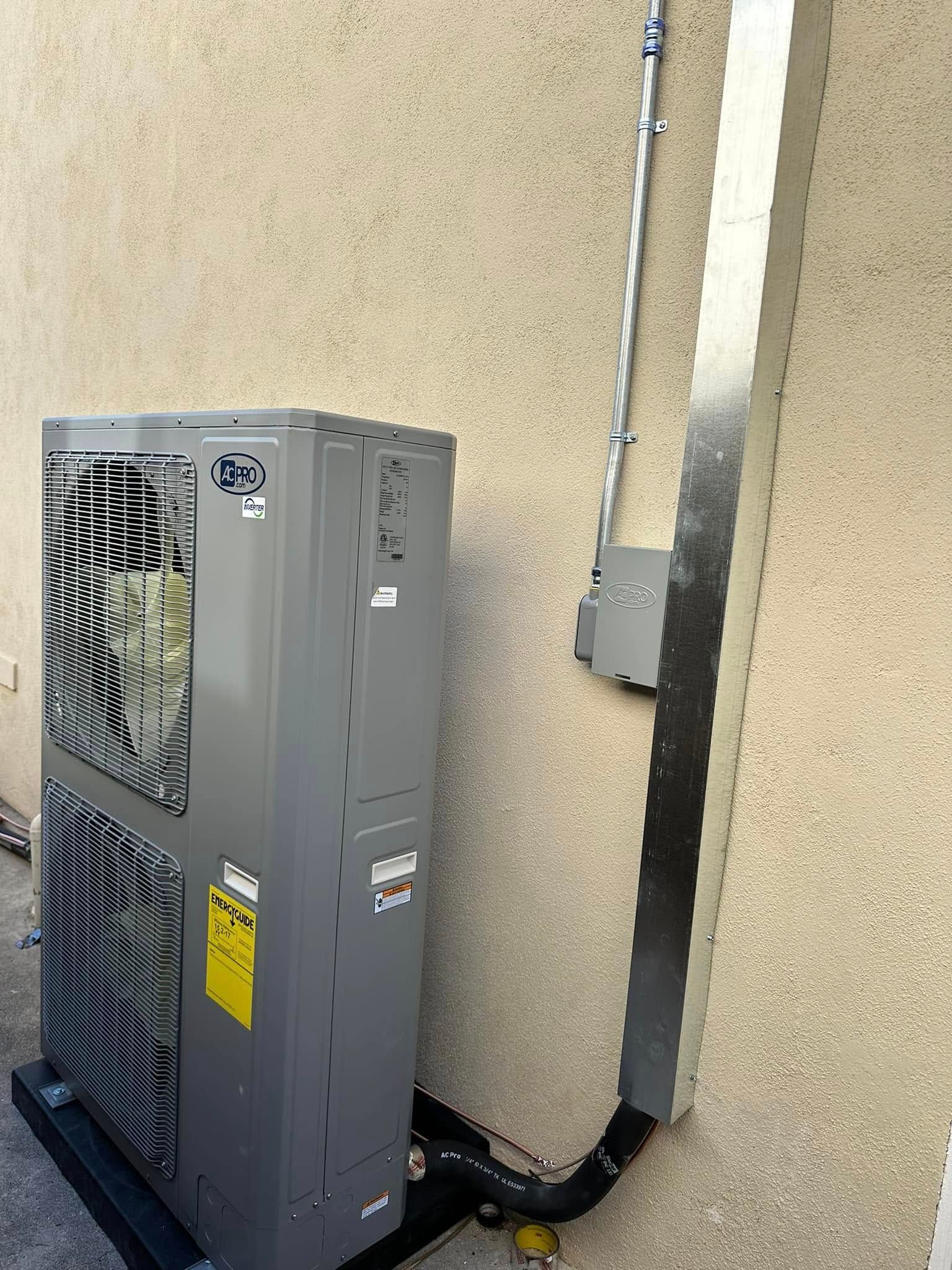 Outdoor HVAC unit beside a stucco wall with conduit and electrical box attached nearby