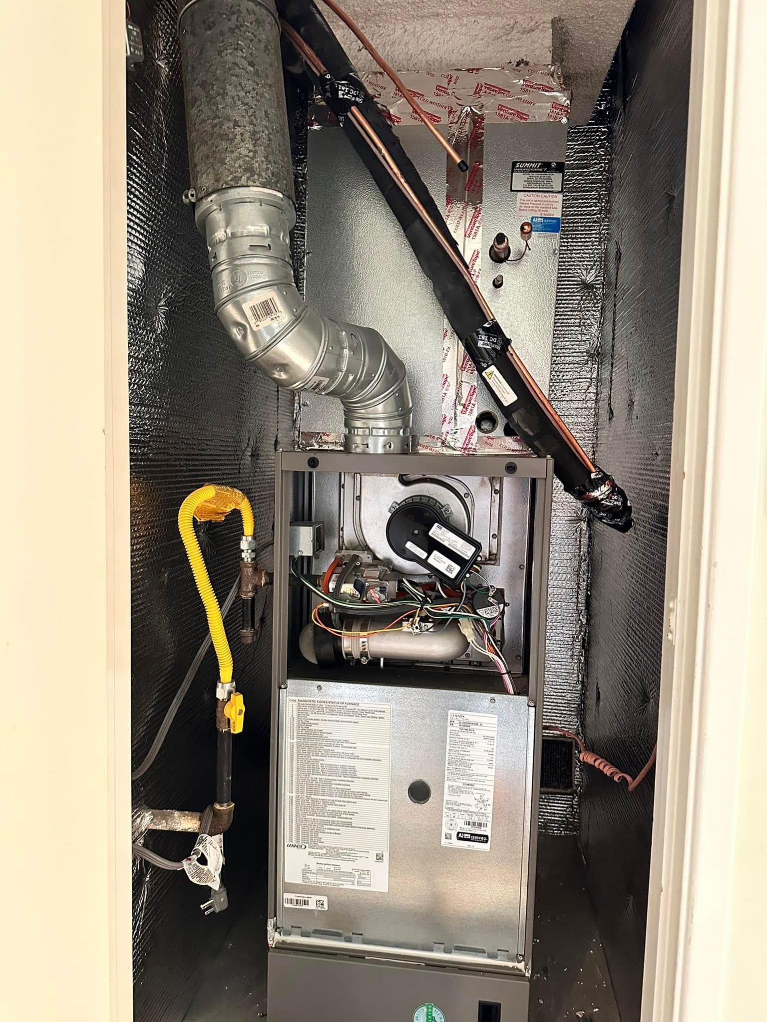Open furnace cabinet in a utility closet with ductwork, wires, and insulation lining the walls.