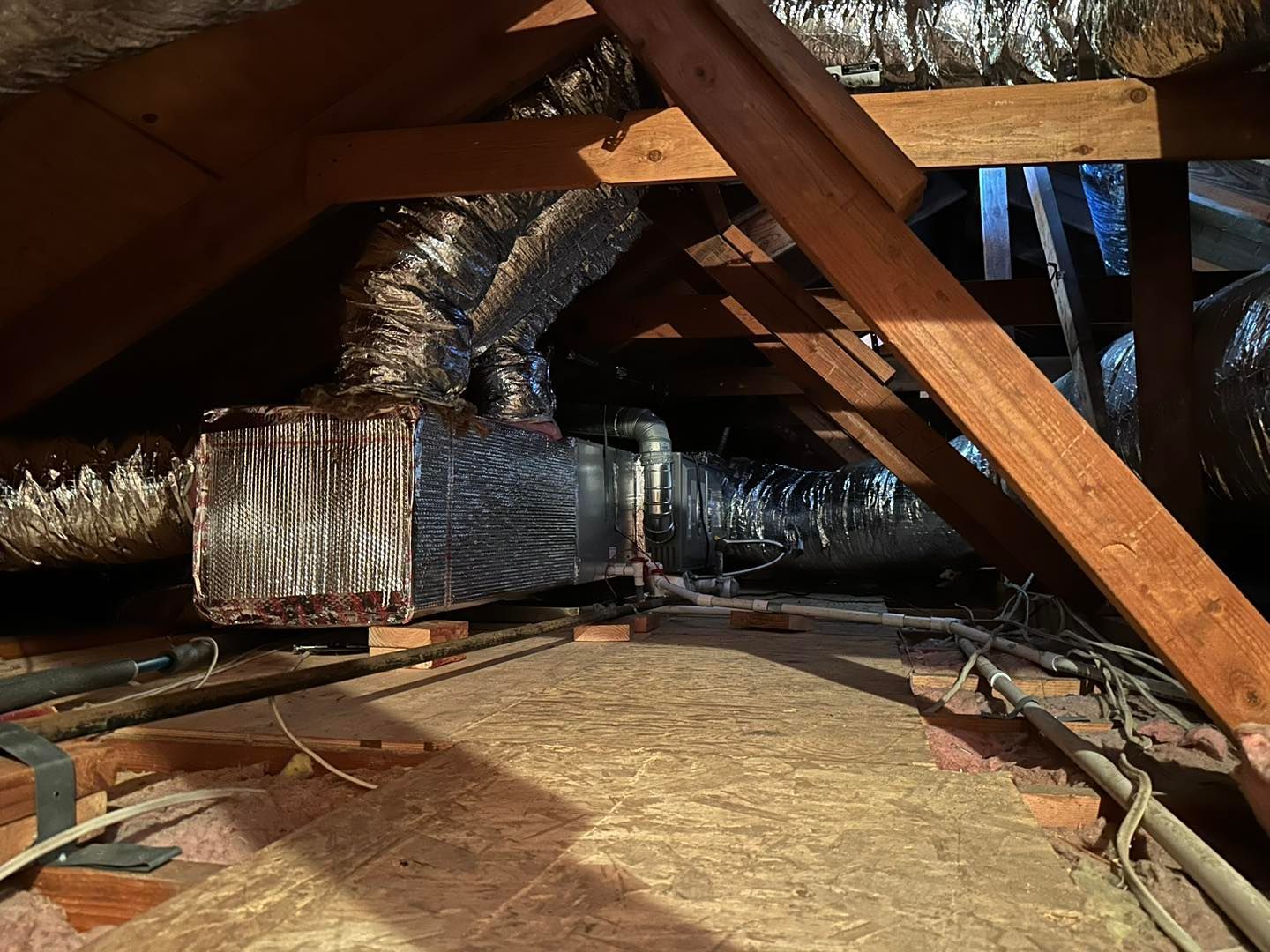 Attic crawlspace with exposed wooden rafters and silver HVAC ducting on the floor and ceiling.