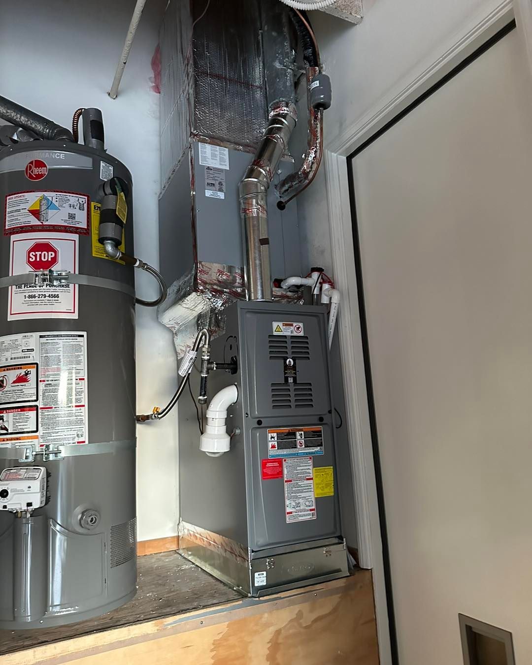 Two gray water heaters in a utility closet with exposed pipes and ductwork