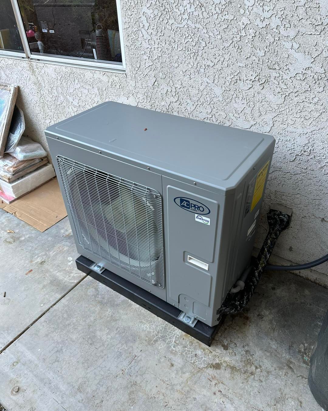 Gray outdoor HVAC unit beside a stucco wall on a concrete patio