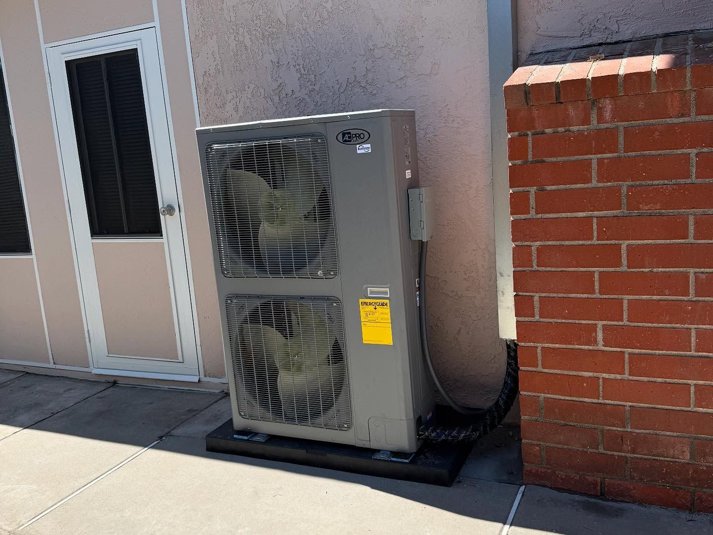 Outdoor HVAC unit beside a brick wall and building door on a concrete pad