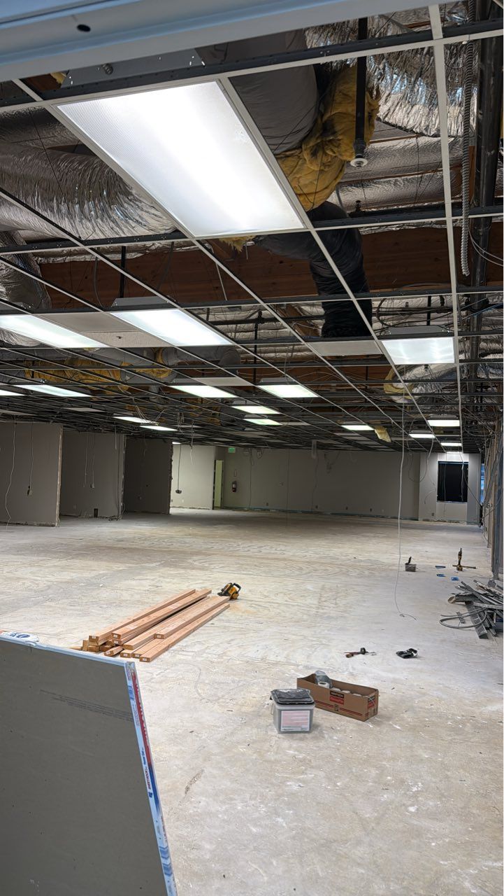 Empty unfinished commercial interior with exposed ceiling, hanging lights, and construction debris on the floor