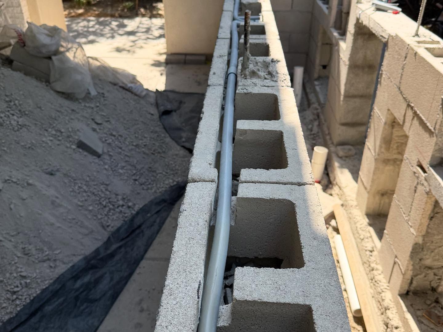 Cinder block wall under construction beside a trench, with a metal pipe running along it
