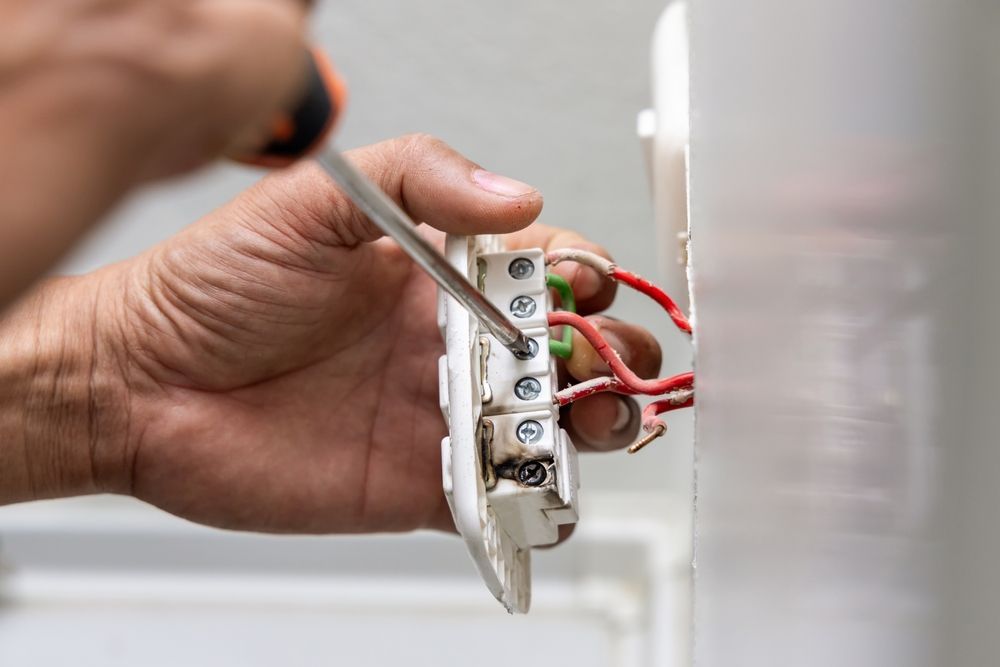 Hand tightening a wall light switch with a screwdriver, exposed red and green wires visible