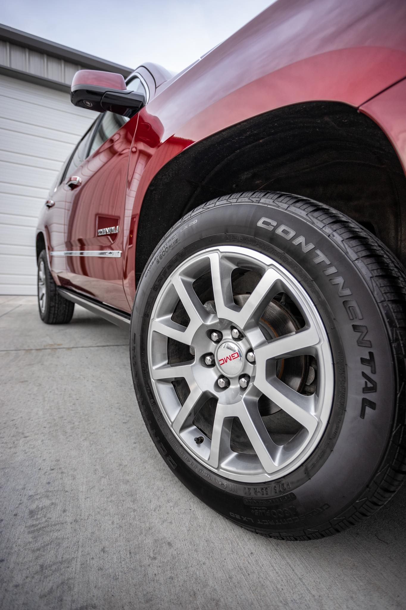 A red car with a continental tire on it is parked in front of a garage.