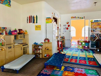 Bright preschool classroom with colorful rugs, toy shelves, books, and child-sized furniture