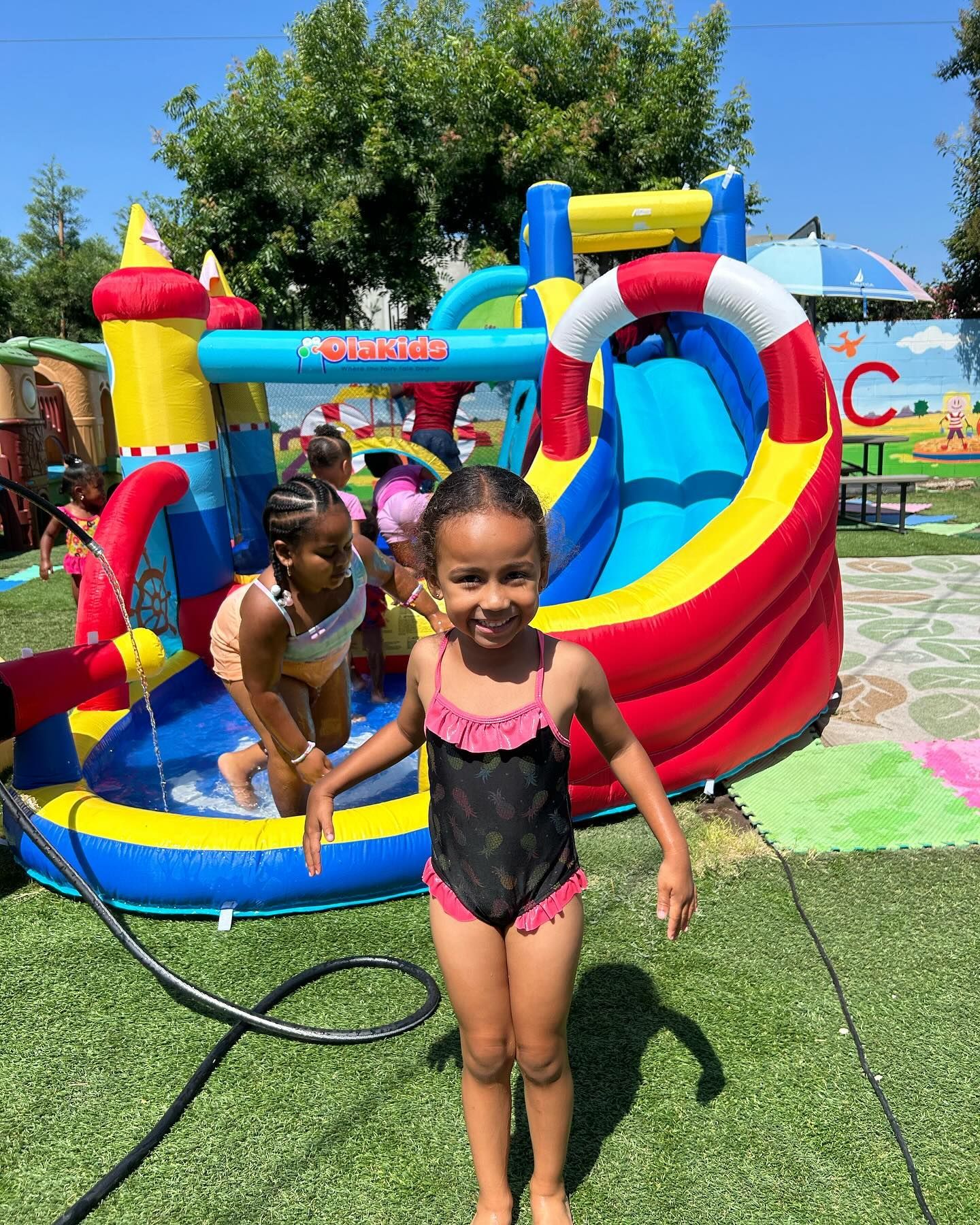 Two children playing on a colorful inflatable water slide in a sunny backyard.