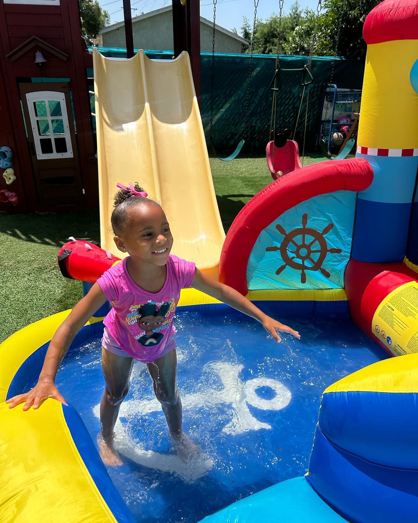 Child playing in a colorful inflatable splash pool, splashing water on a sunny day.