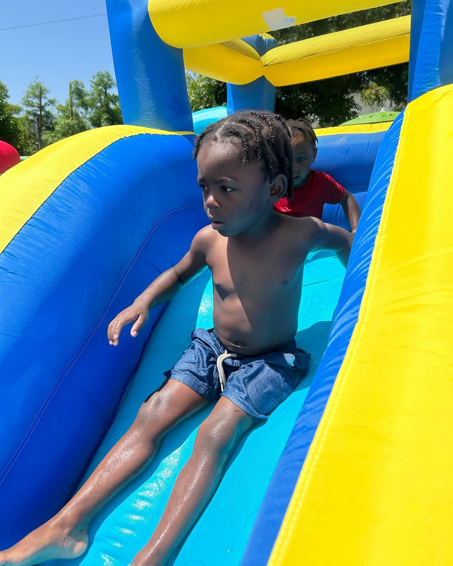 Child sliding down a blue-and-yellow inflatable water slide on a sunny day