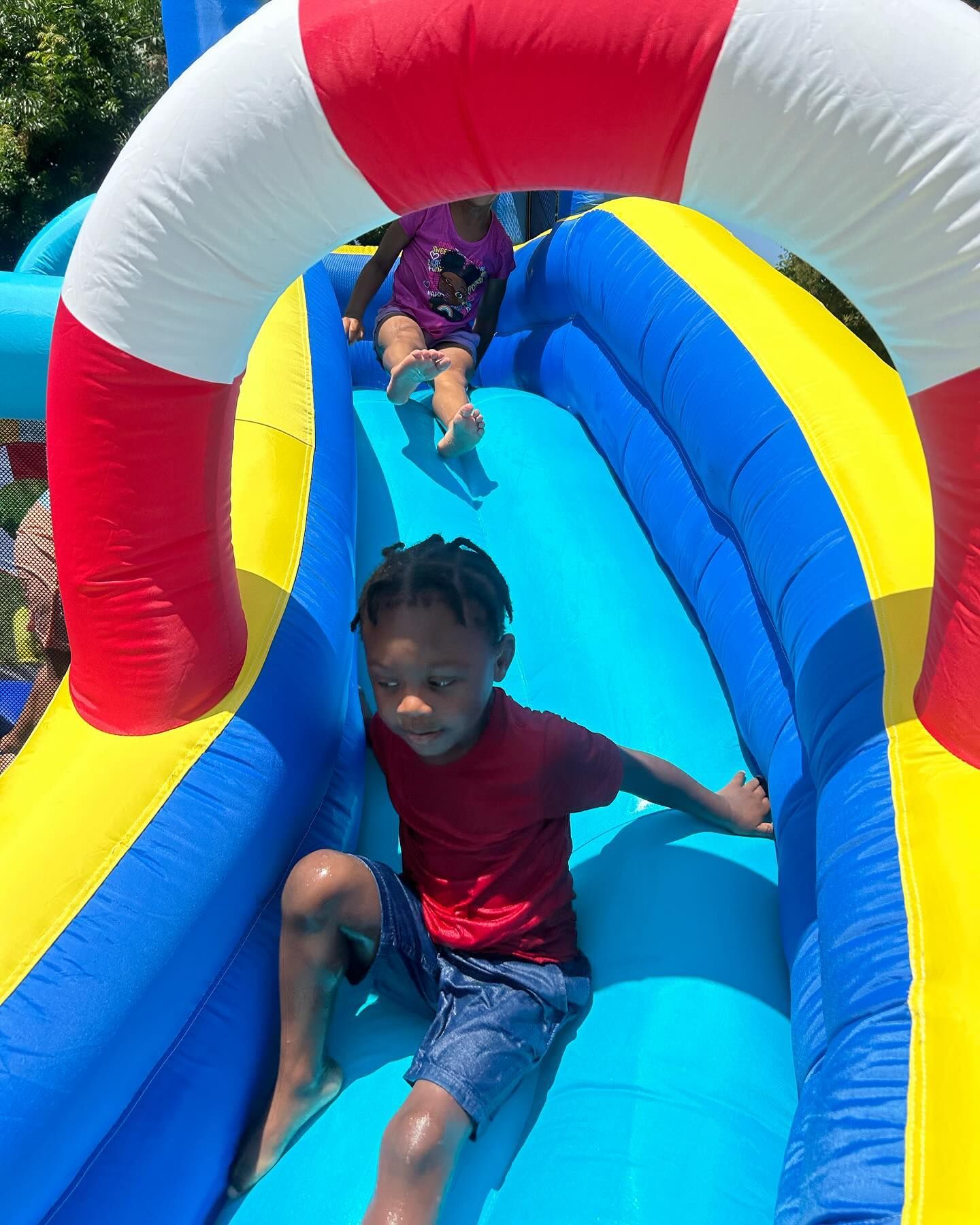 Children sliding down a blue and yellow inflatable water slide under a red and white arch
