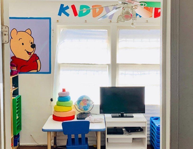 Colorful kids’ room with Pooh poster, rainbow toy, desk, monitor, and blue chair near bright windows