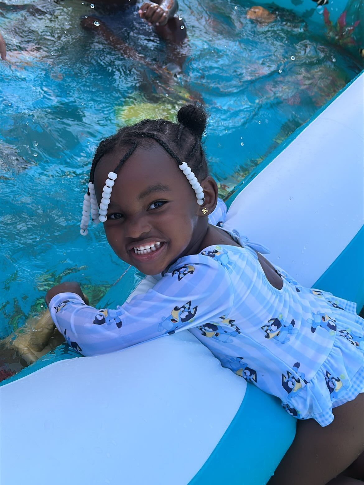 Child smiling on a blue pool float in a swimming pool, wearing a light blue swimsuit