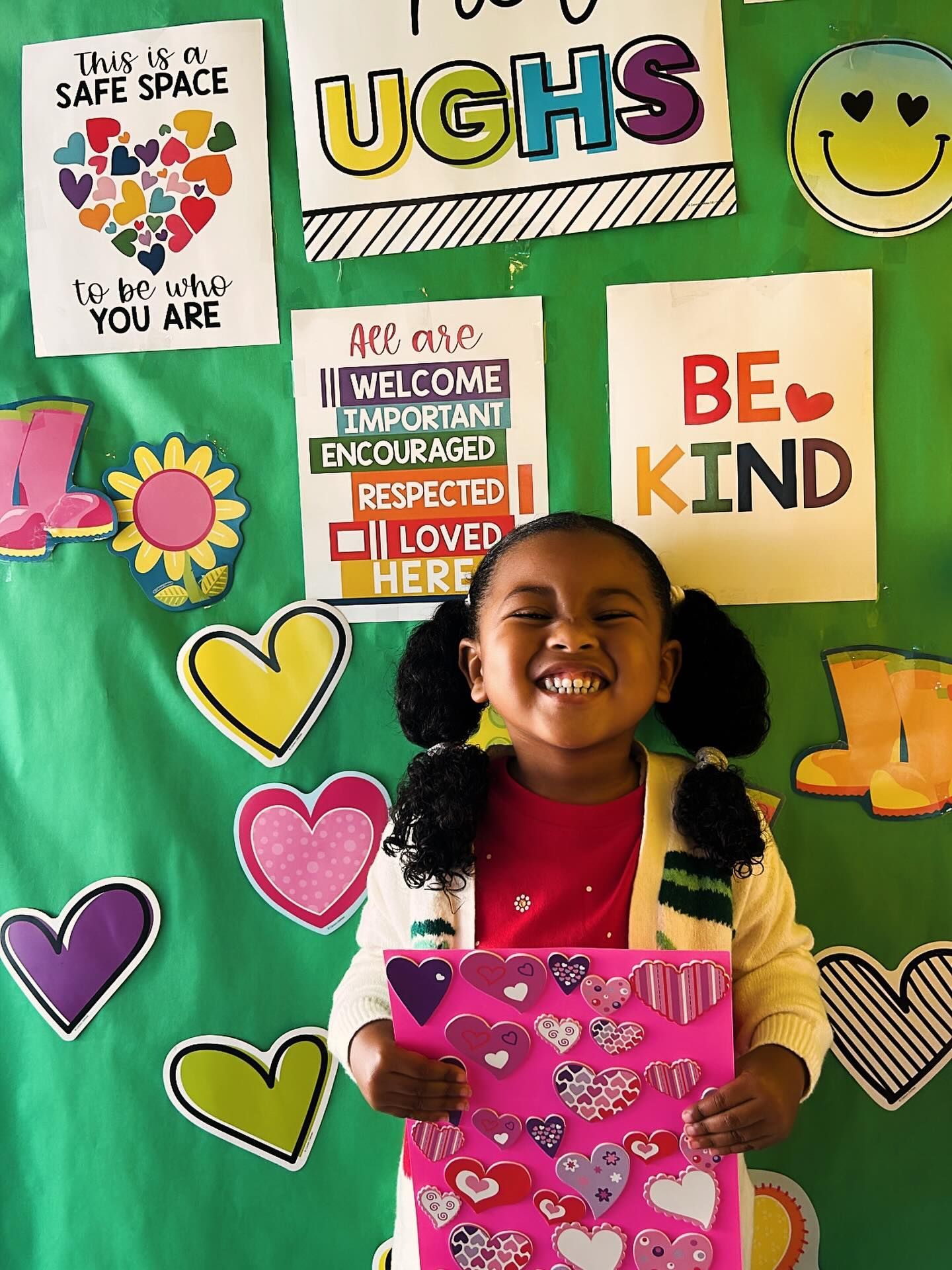 Smiling child holding a pink folder in front of colorful classroom kindness posters