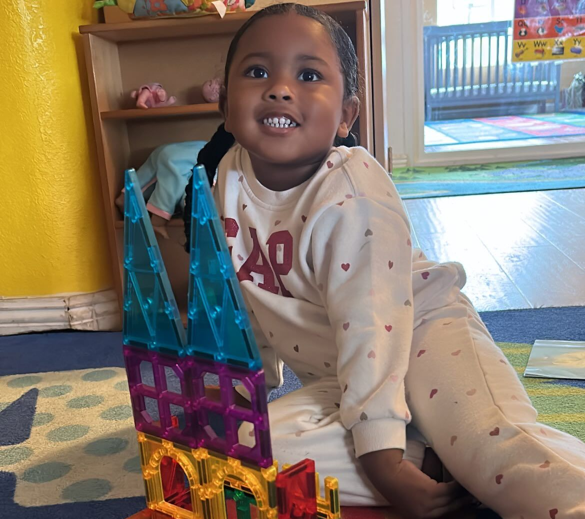 Smiling child on the floor beside colorful magnetic toy towers in a bright room.