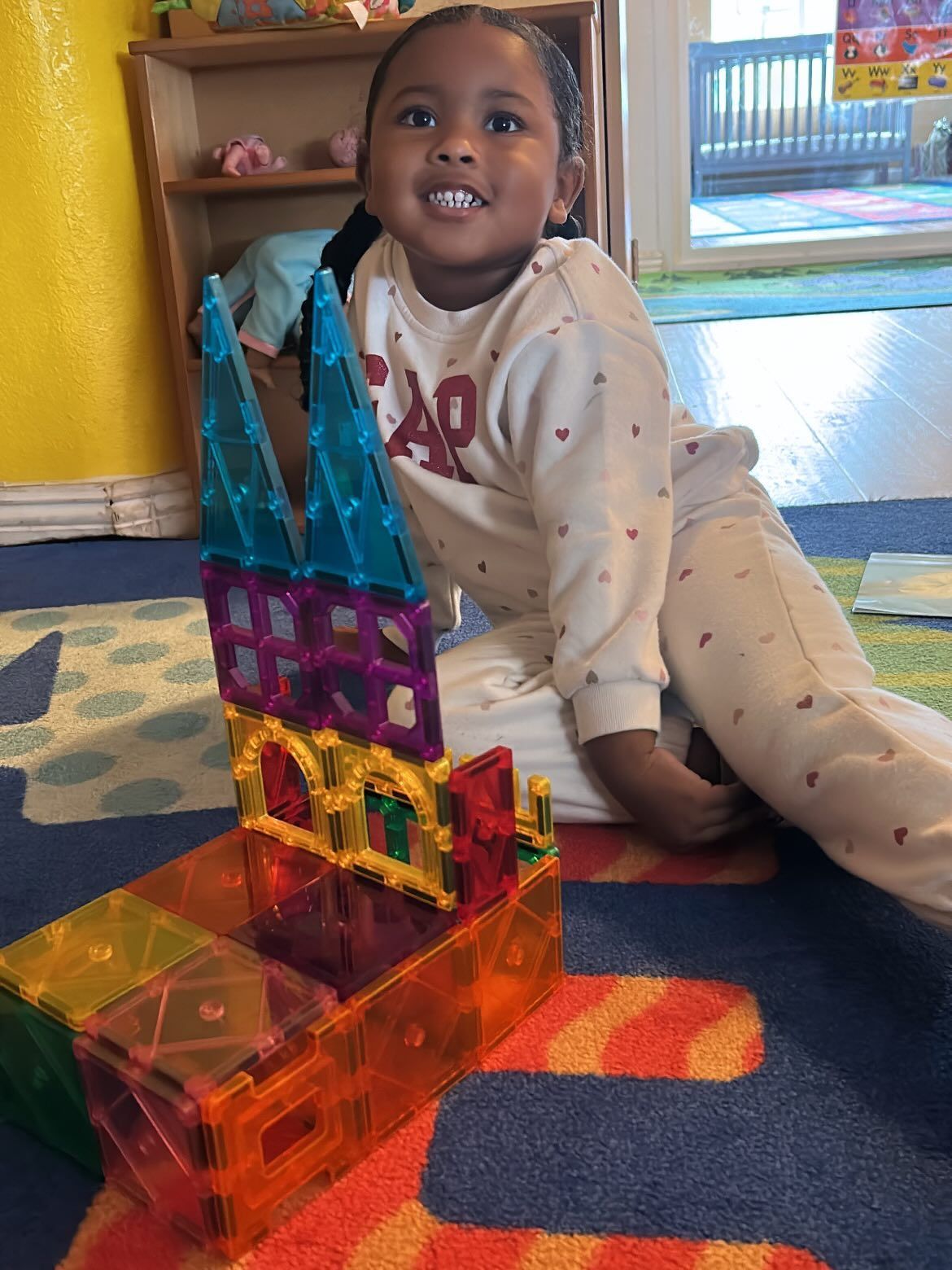 Child kneeling on carpet beside colorful magnetic tile castle in a bright playroom