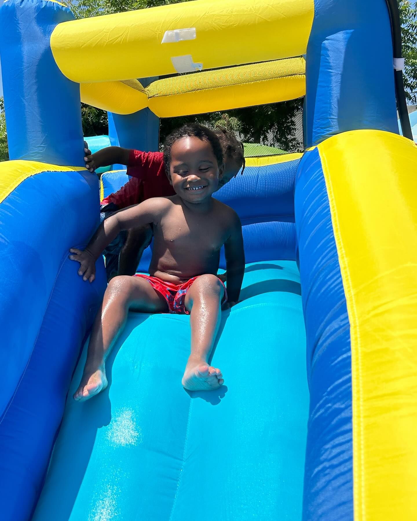Child sliding down a bright blue and yellow inflatable waterslide, smiling in the sun