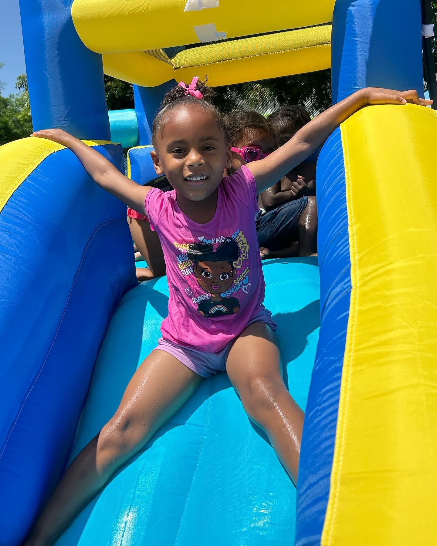 Child smiling on a blue and yellow inflatable slide, sliding down with arms outstretched.