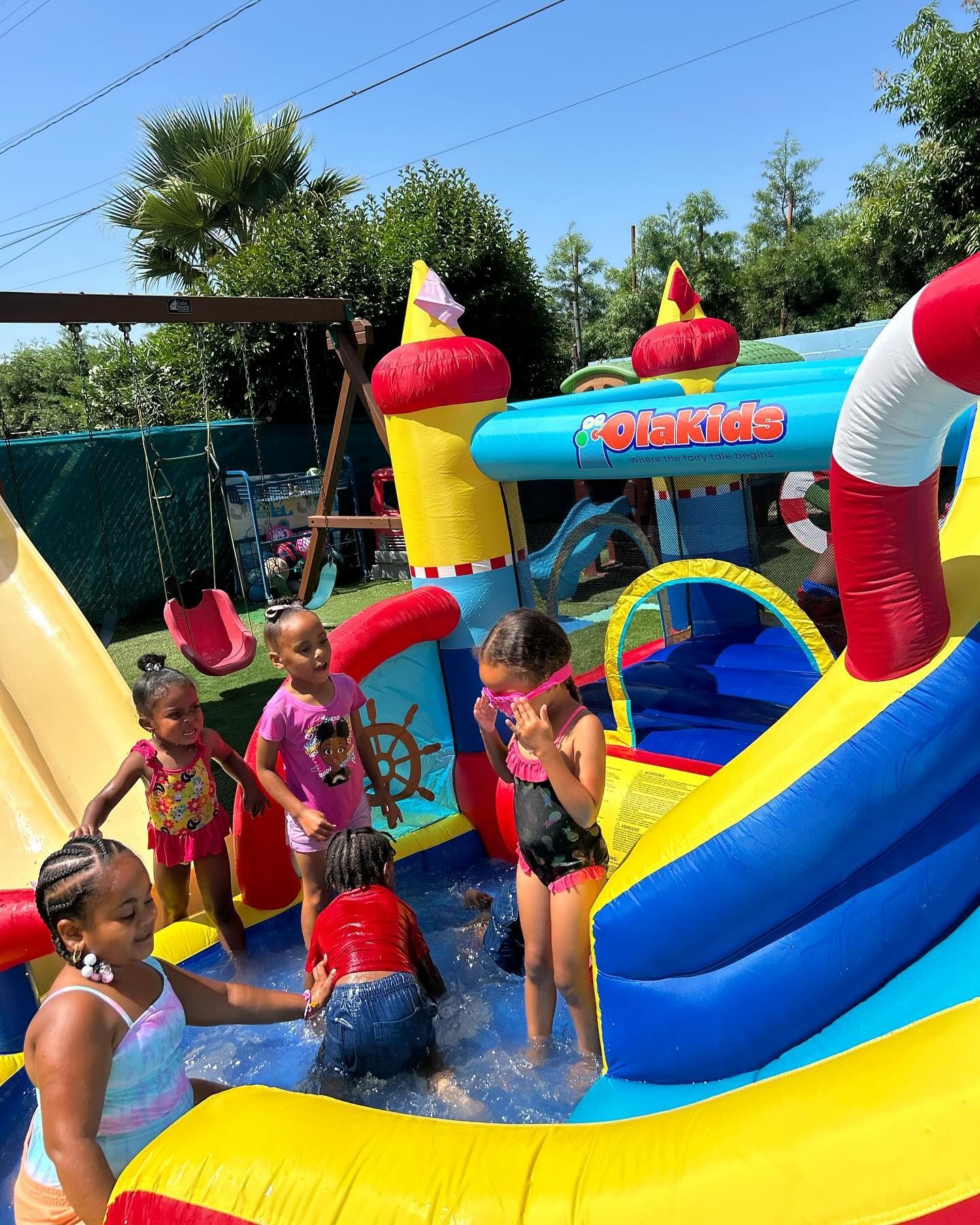 Children playing in a colorful inflatable water slide splash area on a sunny day