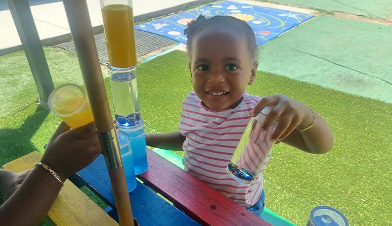 Smiling child holding a small snack at a colorful outdoor picnic table