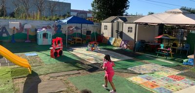 Children play in a colorful fenced playground with tents and toys on a sunny day