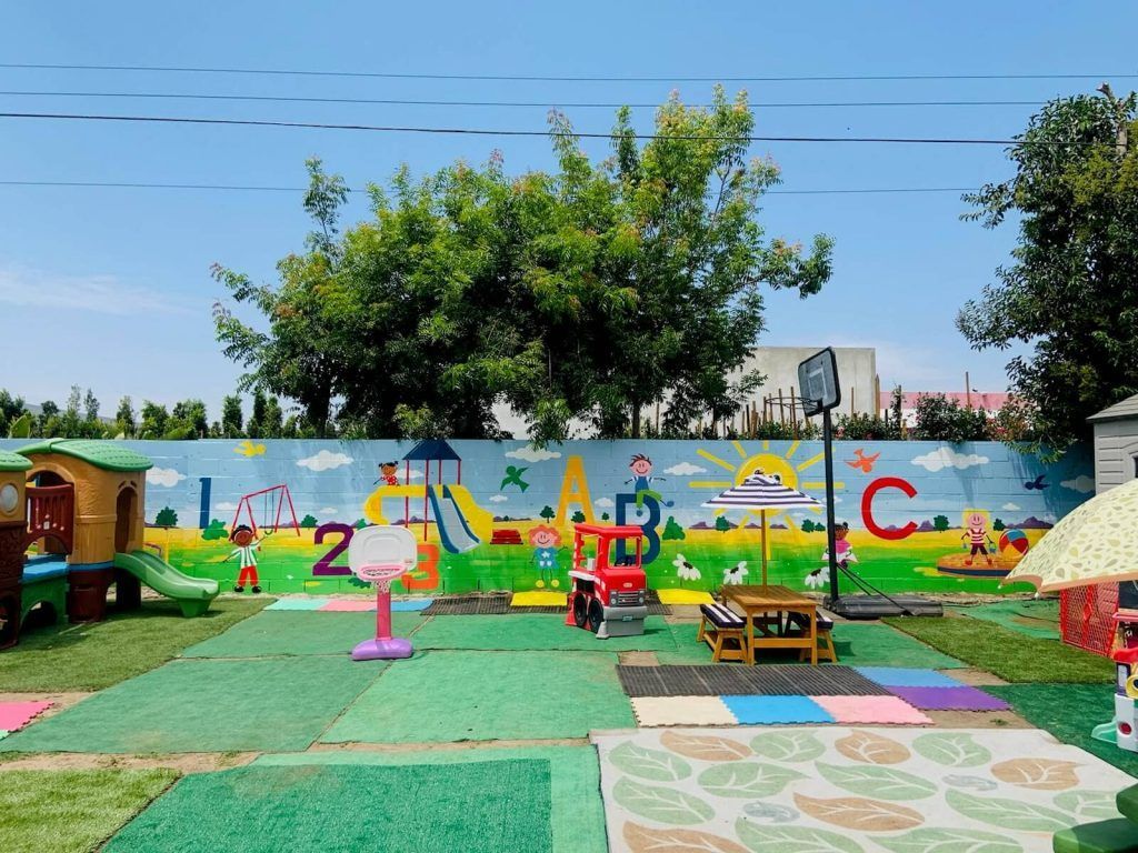 Colorful children’s playground with painted mural wall, slides, benches, and play structures under a blue sky