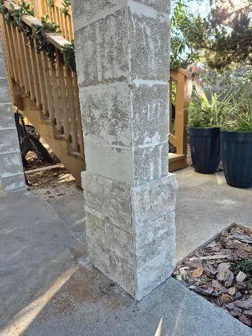 Stone porch pillar beside wooden railing and black planters on a sunny patio