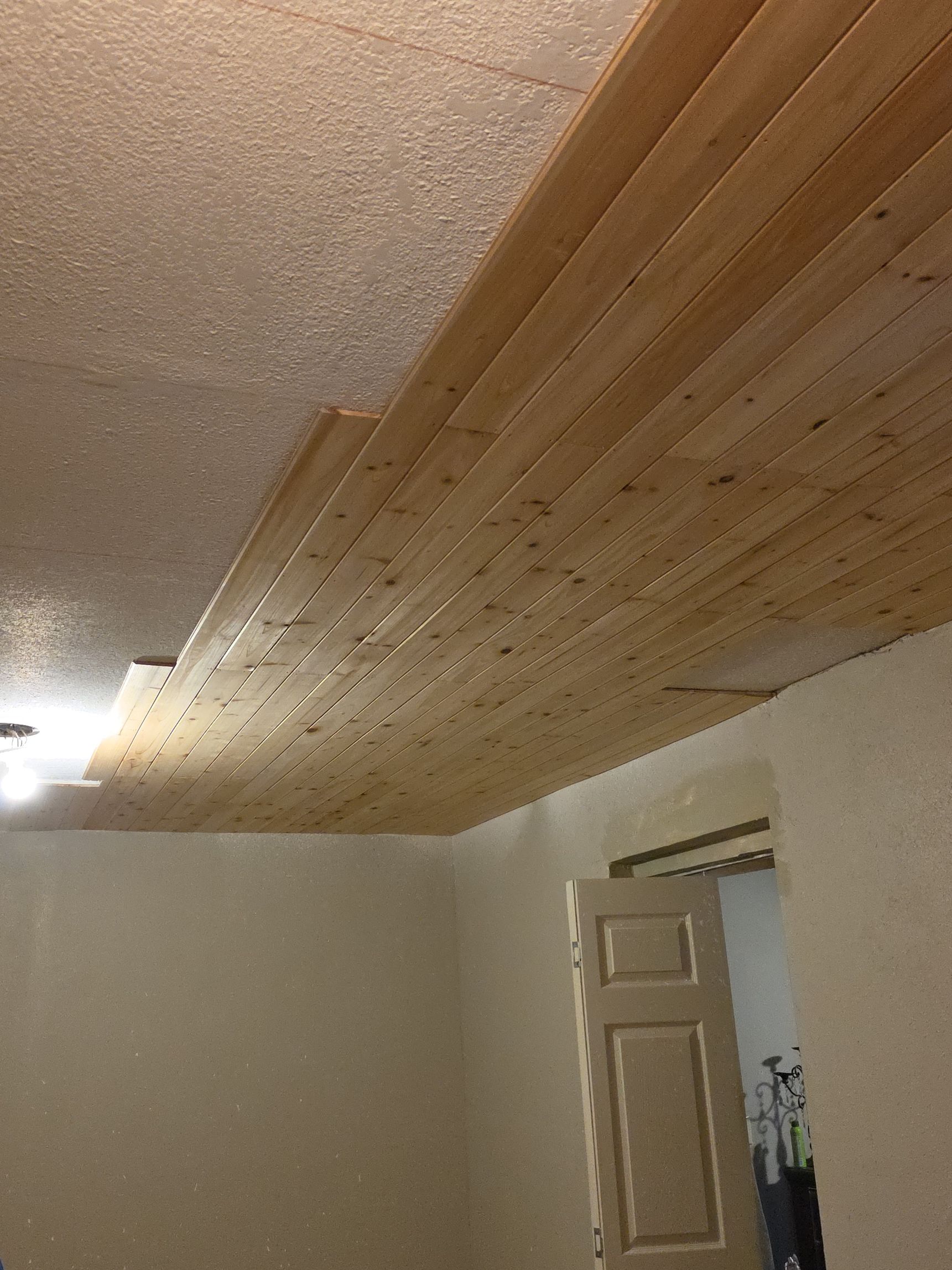 Ceiling covered with wood planks above a room doorway and beige walls