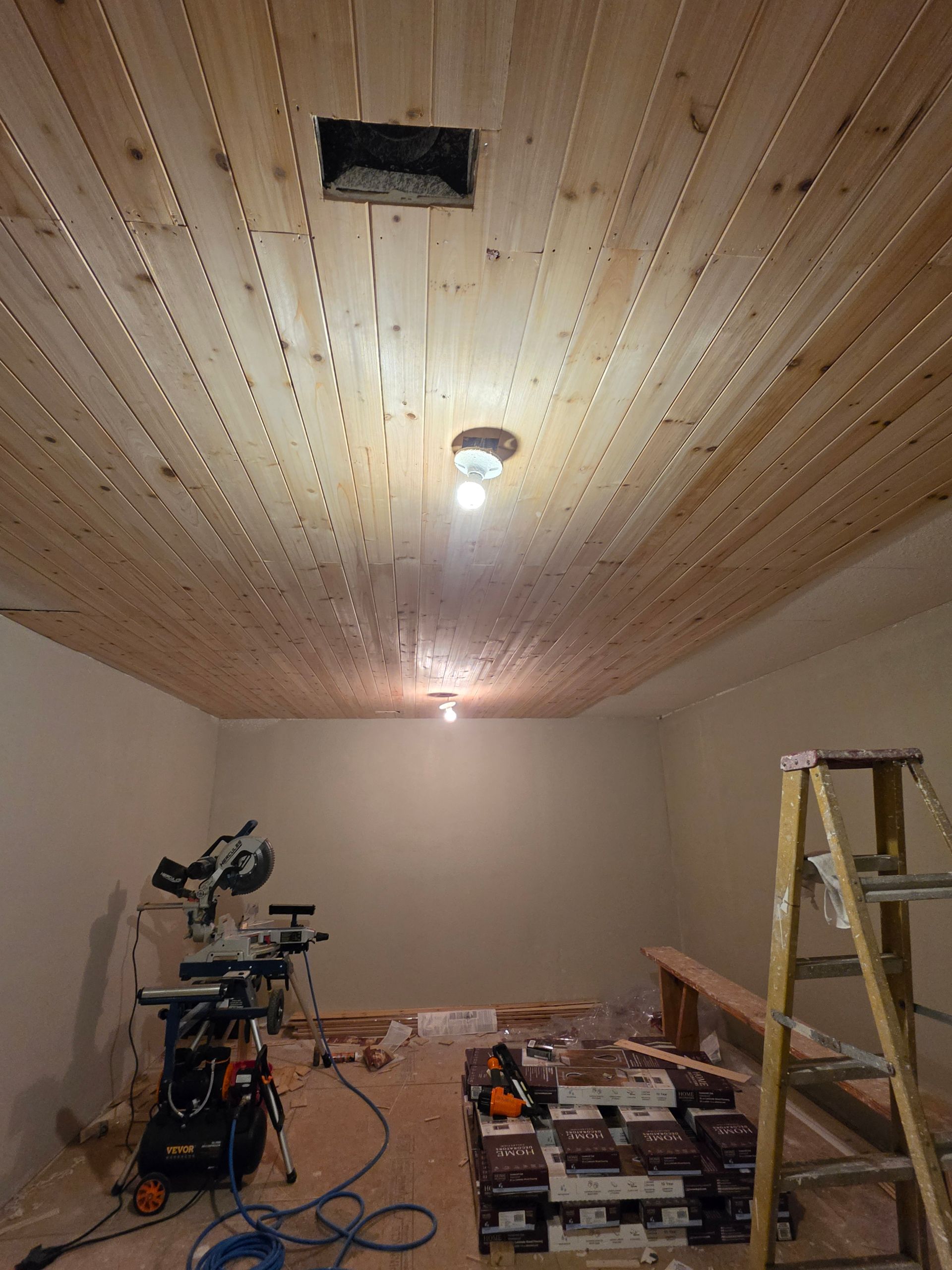 Renovation room with wood-paneled ceiling, ladder, tools, and construction materials scattered on the floor