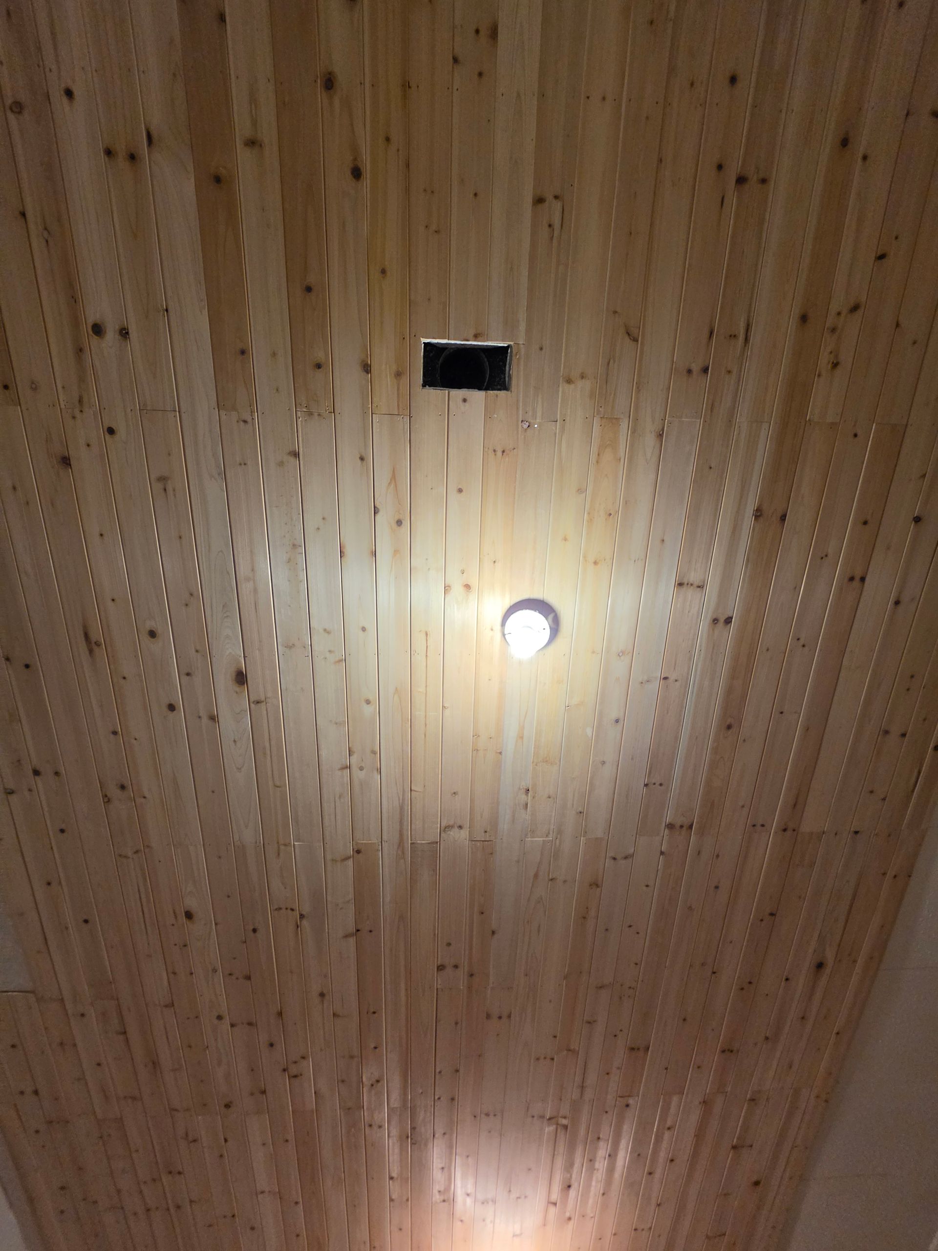 Wooden slatted ceiling with two recessed lights, one brightly lit near the center.