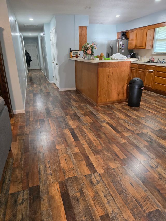 Long hallway with wood-look flooring leading to a kitchen with wooden cabinets and a trash can.